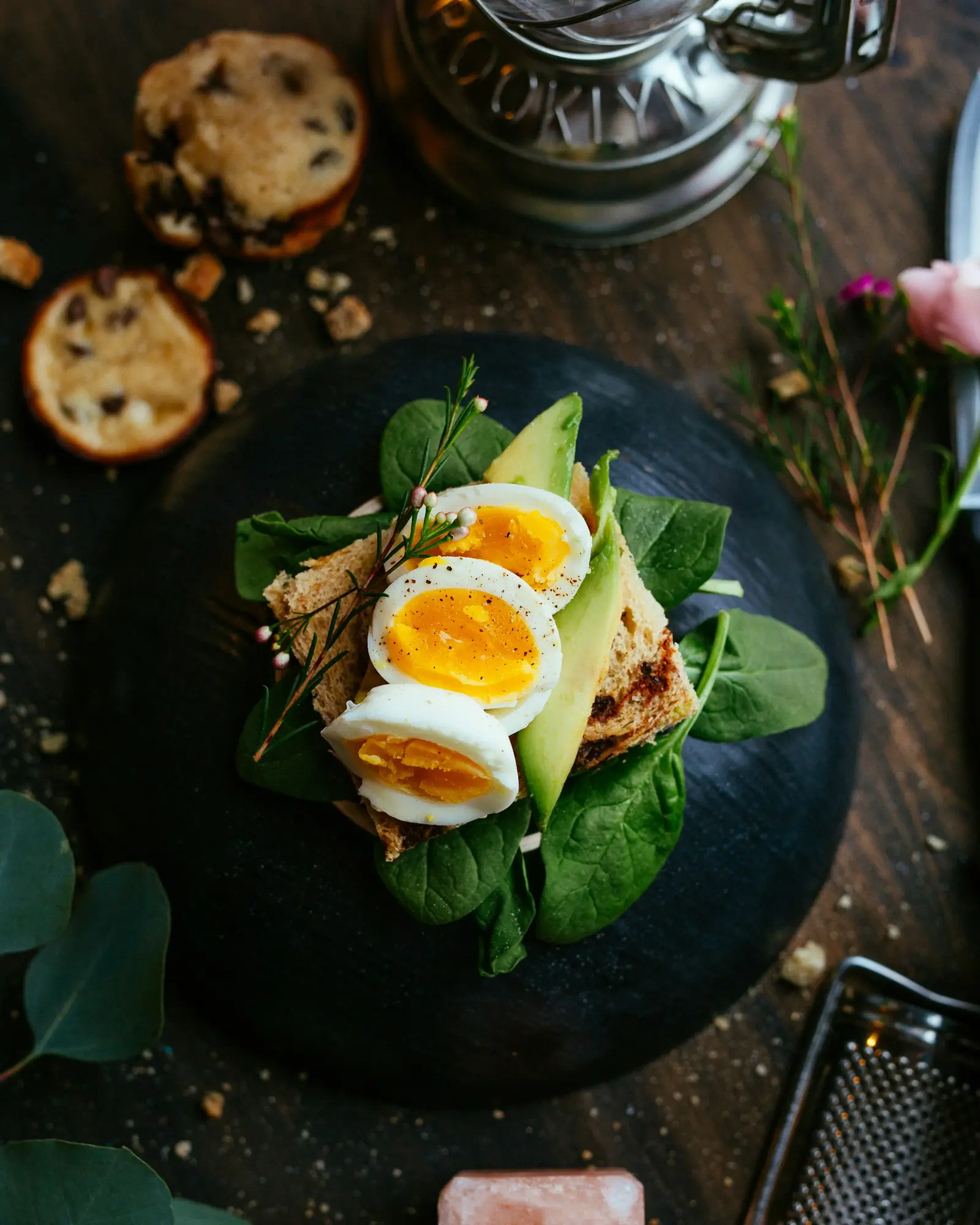 Halved soft-boiled eggs on a dark bowl with avocado and herbs
